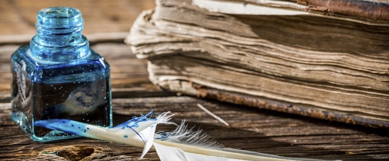Detailed charcoal illustration of a quill, inkwell, and open book on a wooden desk, warm brown and ink-blue tones